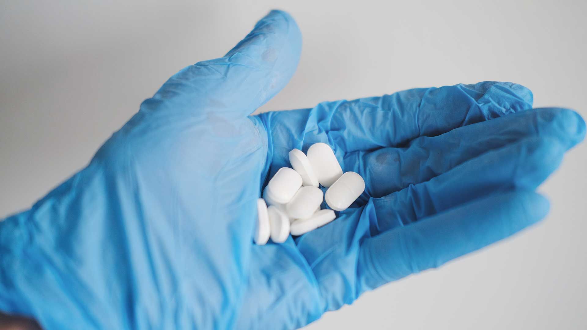 Mano con guante médico sosteniendo pastillas