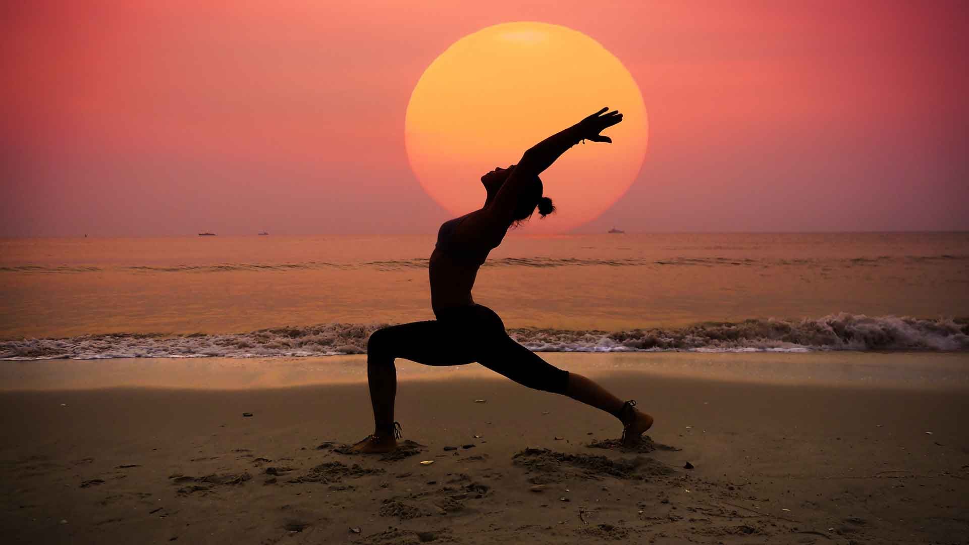Practicando yoga en la playa ante el sol poniente